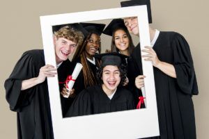 Diverse,Students,Wearing,Cap,And,Gown,Holding,Photo,Frame,Studio